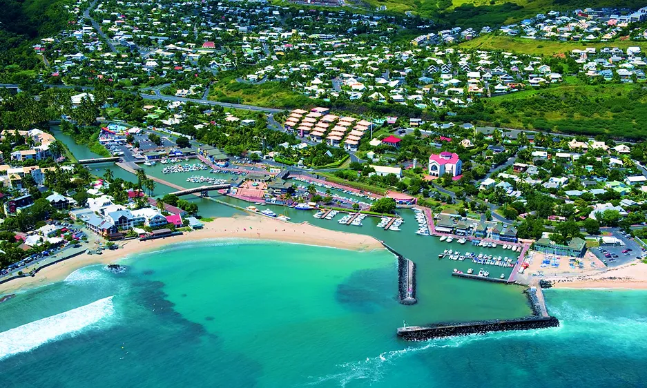 Vue aérienne d'une plage et d'une ville, montrant le littoral et les bâtiments environnants sous un ciel dégagé.